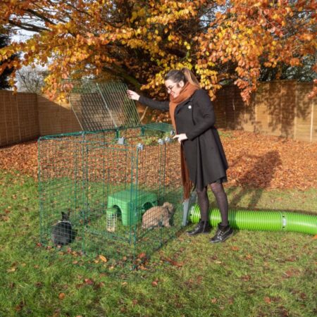 Eine Frau im Herbst im Freien mit zwei Kaninchen in einem Auslaufgehege