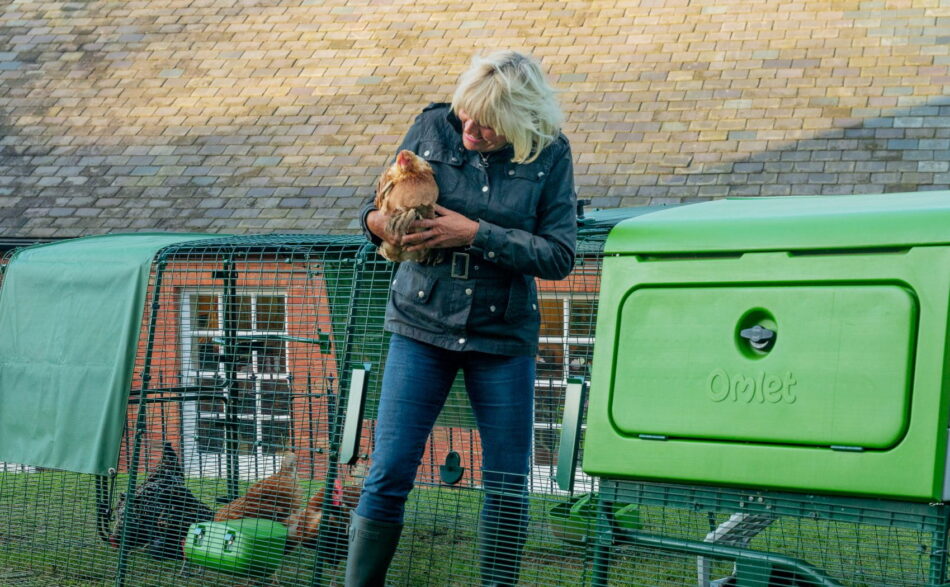 Eine Frau mit einem Huhn auf dem Arm steigt aus dem Eglu Pro Hühnerstallauslauf aus