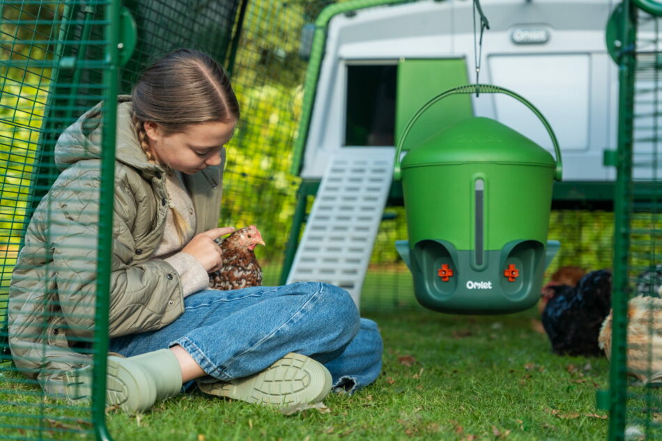 Ein Mädchen hält vorm Eglu Pro Hühnerstall ein Huhn auf dem Arm