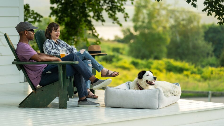 Ein Paar sitzt draußen mit seinem Hund, der auf dem Omlet Hundenest sitzt