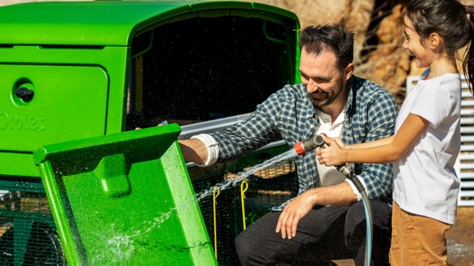 Ein Mann und ein Mädchen reinigen den Omlet Eglu Pro mit einem Gartenschlauch