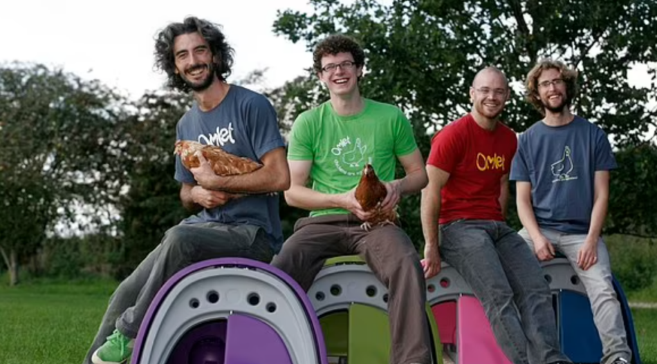 Omlet-Gründer Hanns, James, Simon und Will zur Anfangszeit von Omlet, auf Hühnerställen sitzend und mit Hühnern auf dem Schoß.